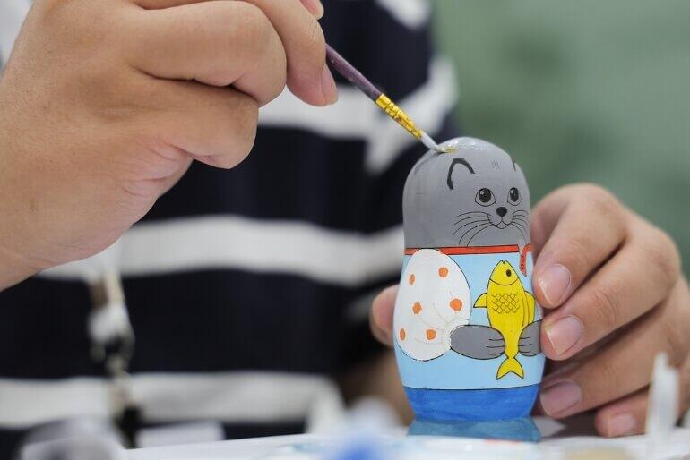 Výběr dětských kroužků. Detailní záběr na ruce malující figurku symbolizuje pestrou nabídku kreativních a výtvarných dílen, které si rodiny mohou vyzkoušet na Kroužkofestu nebo ve Středisku volného času Lužánky. KULTINO*