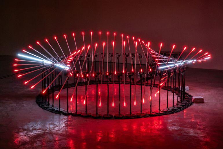 Kinetická světelná instalace tvořená desítkami červeně zářících prvků uspořádaných do dynamického kruhu v potemnělém prostoru, Festival PROTOTYP, Brno. KULTINO*