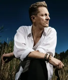 Zpěvák Ondřej Ruml v bílé košili sedí v rákosí pod tmavým nebem, vizuál vánočního koncertu Zapomenutý příběh. KULTINO*
