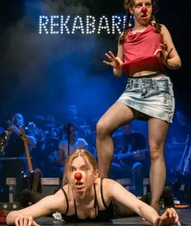 Dvě herečky s červenými klaunskými nosy na jevišti, v pozadí kapela a svítící nápis Rekabaret. Večer Re:Kabaret. KULTINO*