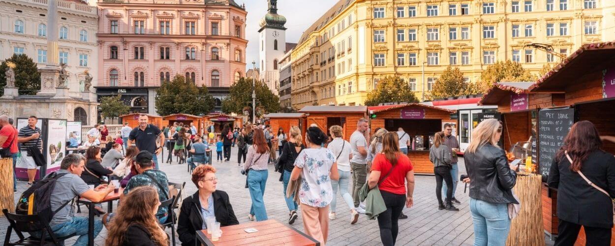 Premiérové burčákové slavnosti na náměstí Svobody v Brně. Skupinky lidí si u dřevěných stánků v historickém centru města s úsměvem užívají první letošní burčák. KULTINO*