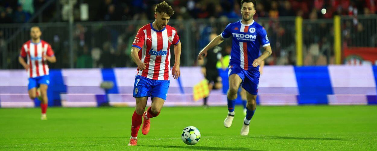 Dramatický souboj o míč během vyostřeného brněnského fotbalového derby. Hráči favorizované Zbrojovky a posíleného Atrisu bojují na trávníku plném emocí před burácejícími tribunami. KULTINO*