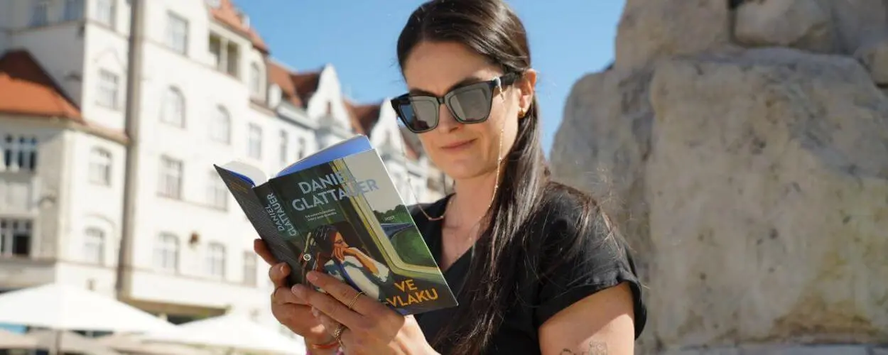 Mladá žena se slunečními brýlemi sedí na prosluněném náměstí v centru Brna a je začtená do knihy. Veřejná čtení a literární besedy lákají lidi do ulic během akce Noc literatury. KULTINO*