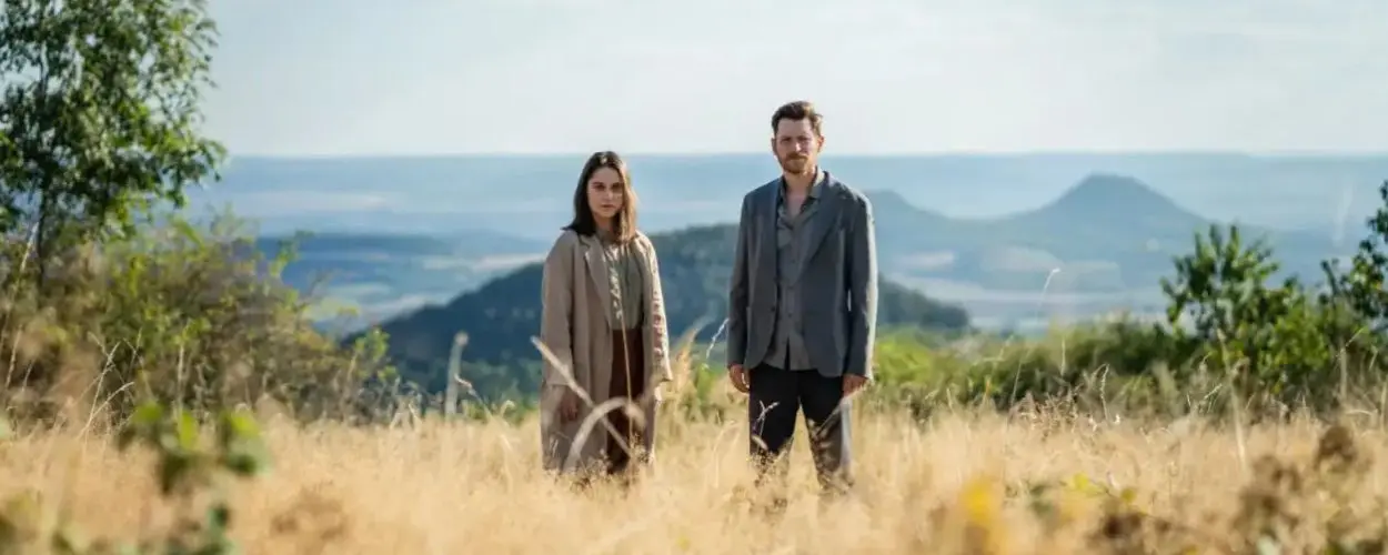 Judit Pecháček a David Švehlík jako Agnes a Martin stojí ve vysoké suché trávě nad krajinou kopců ve filmu Wirbel. KULTINO*
