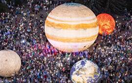 Obrovský dav návštěvníků se svítícími telefony obdivuje obří svítící modely planet, včetně Jupitera a Země, na brněnské Kraví hoře během Festivalu planet. KULTINO*