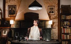 Představení Delikatesa od Mikro teatro. Zaskočený herec s ubrouskem kolem krku sedí u prostřeného stolu v netradičním divadelním prostoru opuštěného brněnského bytu plného knih. KULTINO*