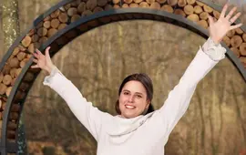 Radostná žena s rozpaženýma rukama pod dřevěnou branou na Naučné stezce svatého Antoníčka z projektu Dáme na vás v Brně. KULTINO*