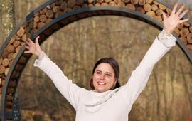 Radostná žena s rozpaženýma rukama pod dřevěnou branou na Naučné stezce svatého Antoníčka z projektu Dáme na vás v Brně. KULTINO*