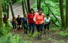 Skupina lidí stoupající lesním terénem s chodeckými holemi při lekci Nordic walkingu. KULTINO*